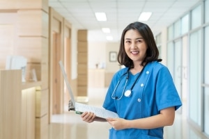 Asian nurse smiling with paperwork in a hospital hallway