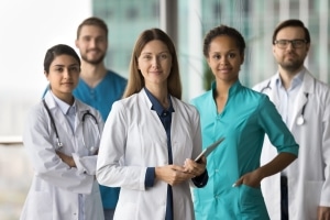 Smiling group of medical professionals wearing scrubs and white coats